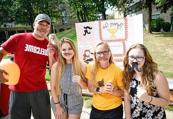 Four Fisher students hold up mustaches on a stick.